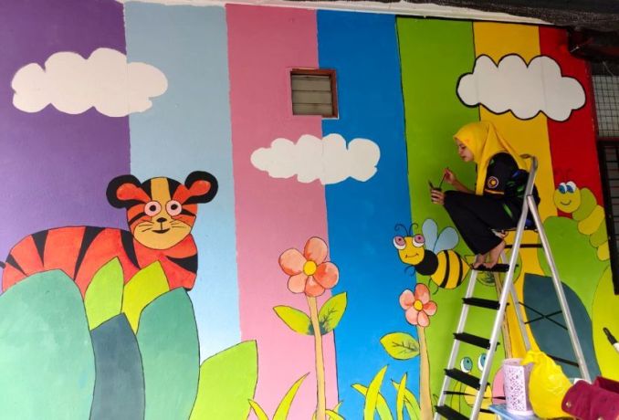 Cikgu Ayu membantu melukis mural di dinding sekolah yang diajarnya.